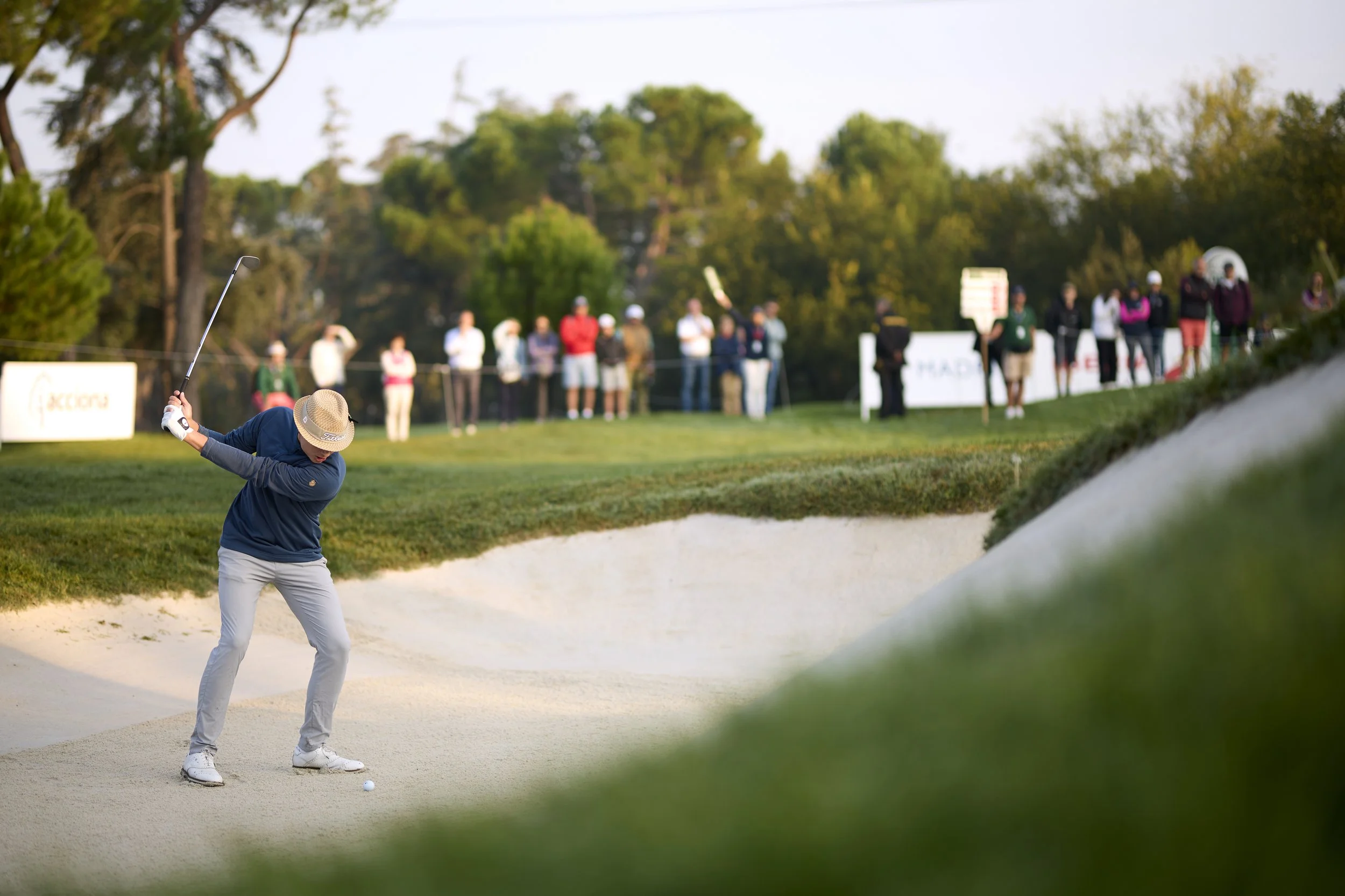 Jugador de golf en una arena de golf, a punto de hacer un golpe en un hoyo, con espectadores en el fondo observando