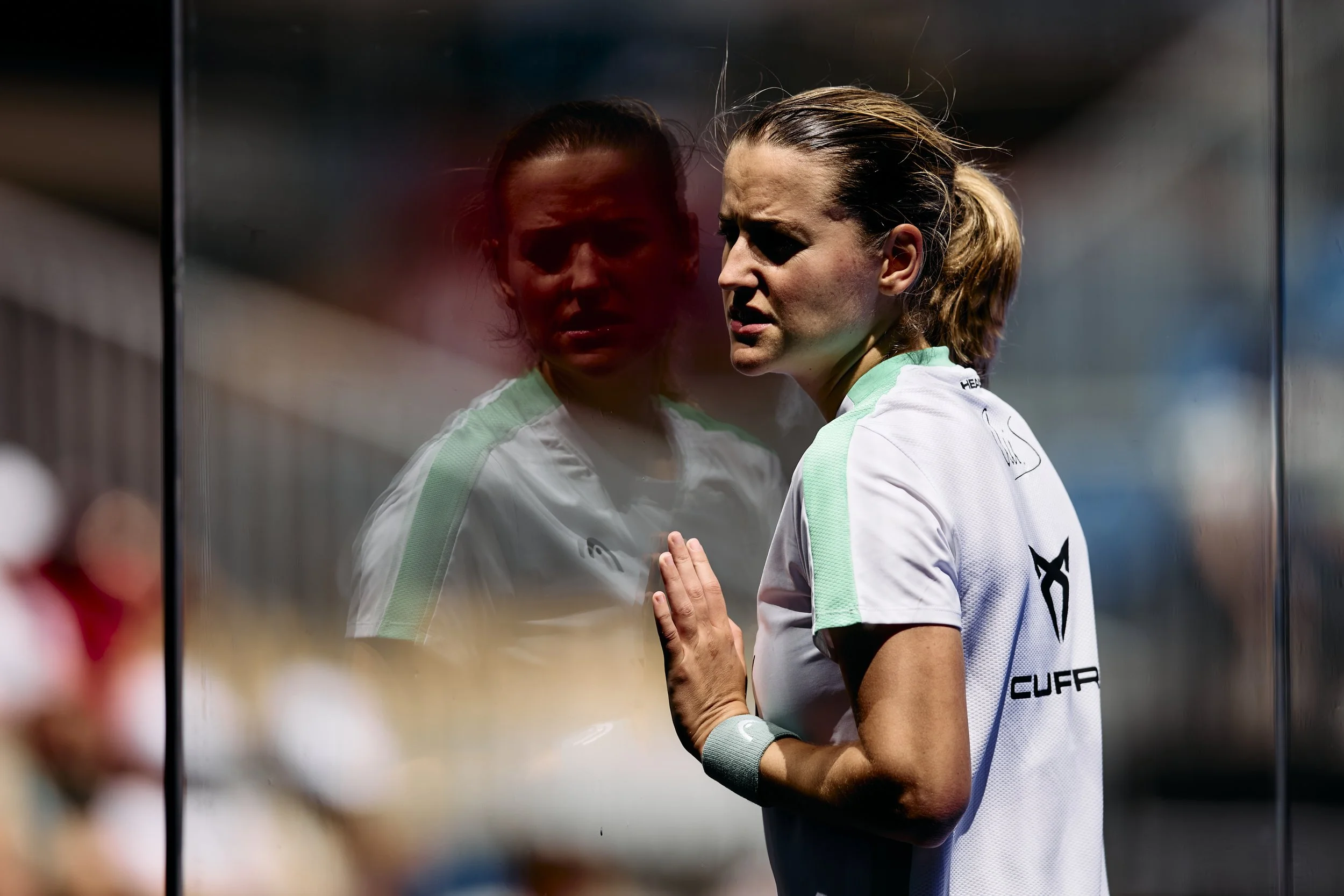 Una mujer atleta mira desde un lado mientras se apoya en un cristal, sus reflejos y expresión de concentración en un entorno deportivo.