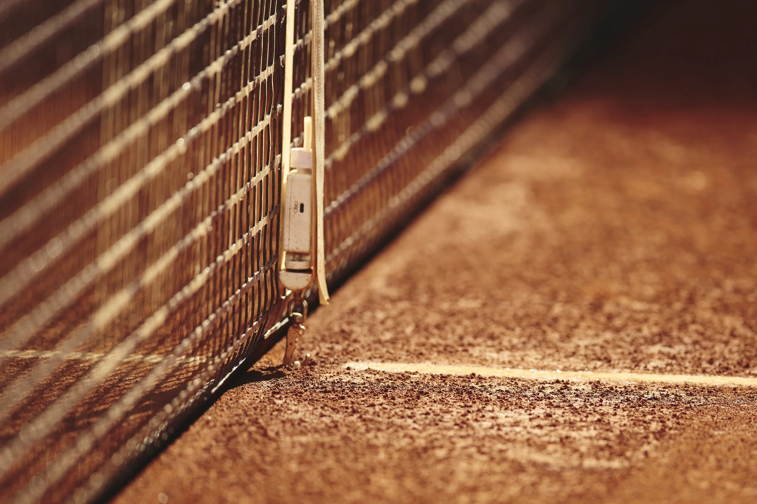 Cerca de una red de tenis en una cancha de arcilla, se puede ver el cierre de la red y la línea lateral marcada en la superficie