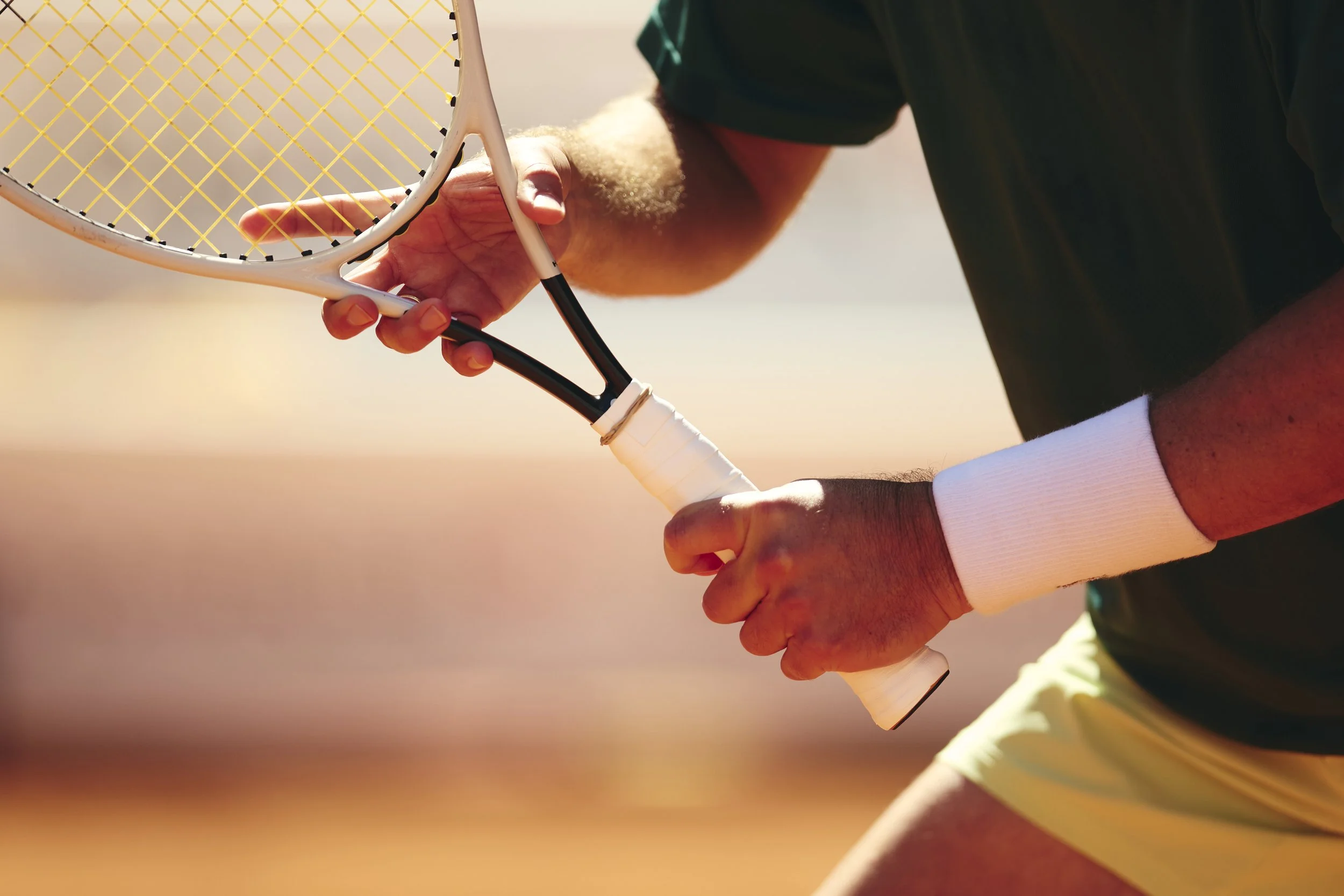 Persona ajustando una raqueta de tenis en una cancha al atardecer.