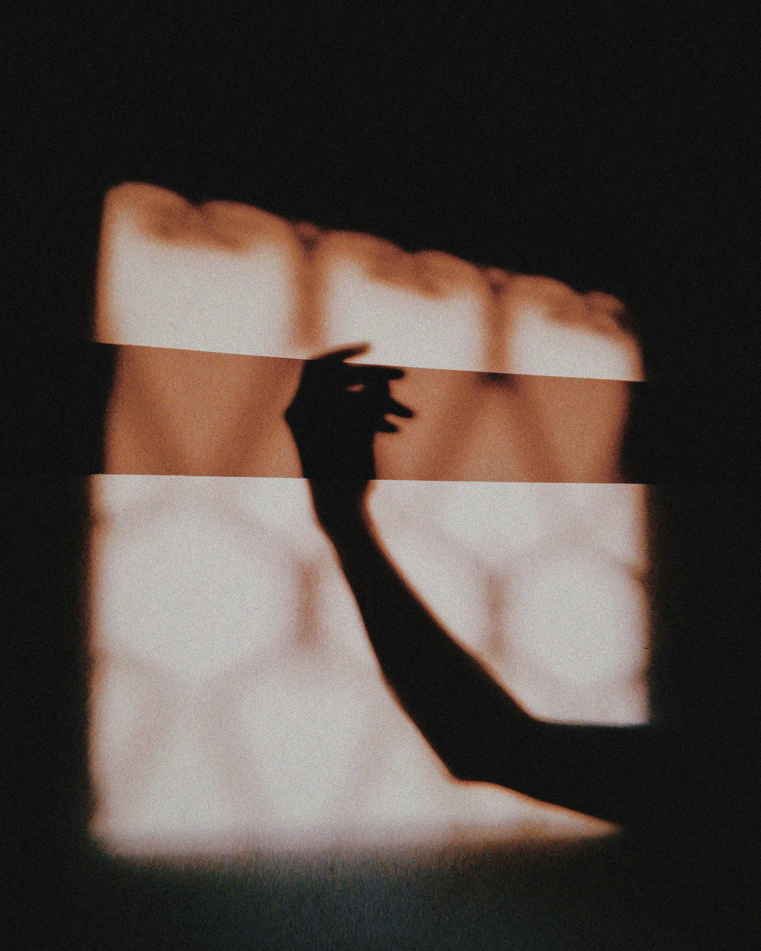 A shadow of a hand with outstretched fingers is cast on a warm, patterned background, creating a mysterious and artistic atmosphere.