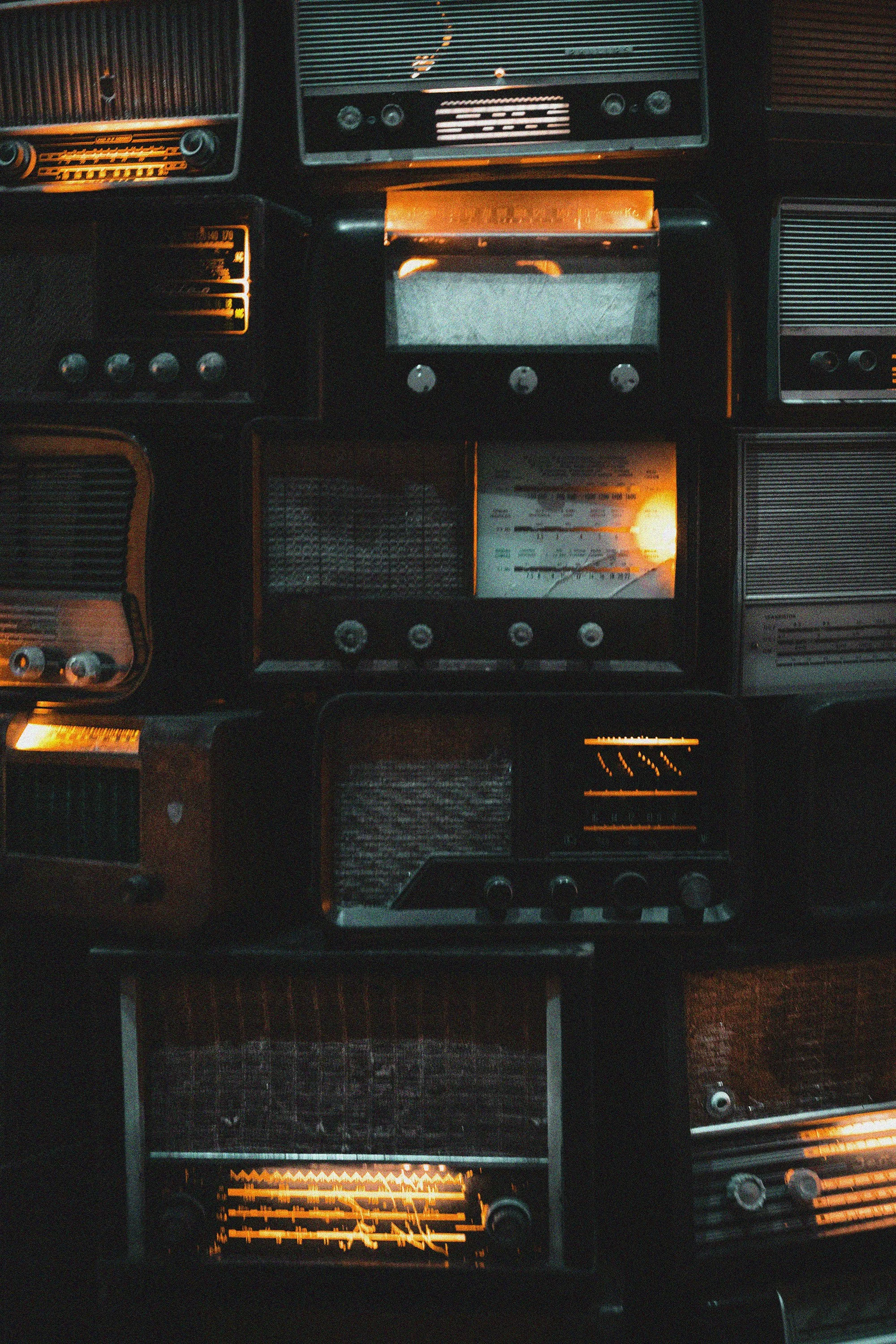 A collection of vintage radios stacked together, dimly lit with a warm, nostalgic glow. The scene evokes a sense of history and timelessness.