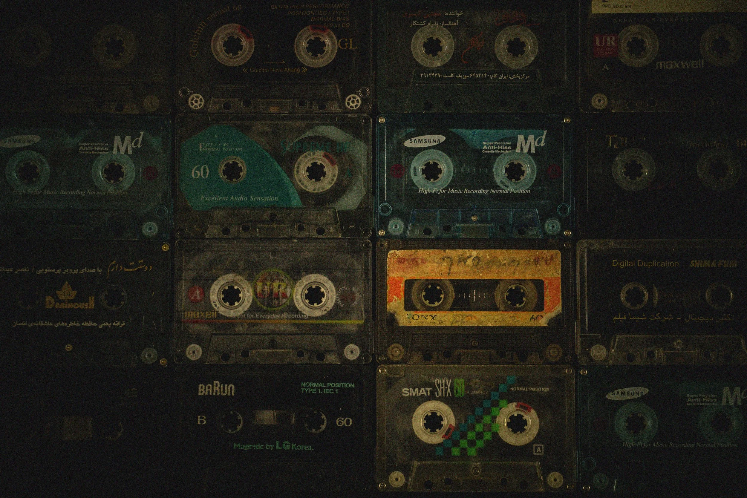 A wall of vintage cassette tapes with various designs and labels. The mood is nostalgic, evoking a sense of retro audio technology.