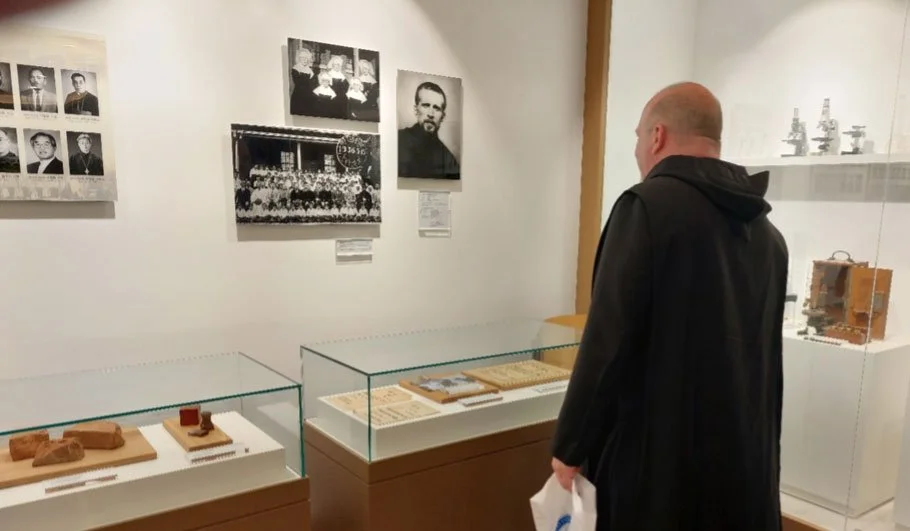 A man dressed in black is photographed from behind in a museum setting looking at the various historical displays.