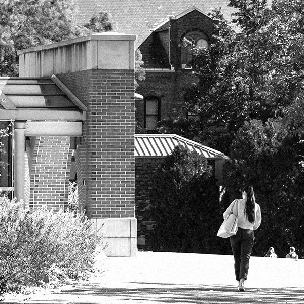photo from behind a student walking on campus toward the buildings.