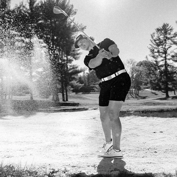 Photo of a golfer hitting a golf ball from a sand trap.