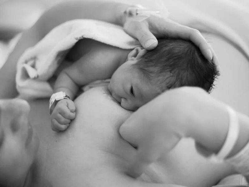 A newborn baby being held on a mother's chest in a hospital setting.