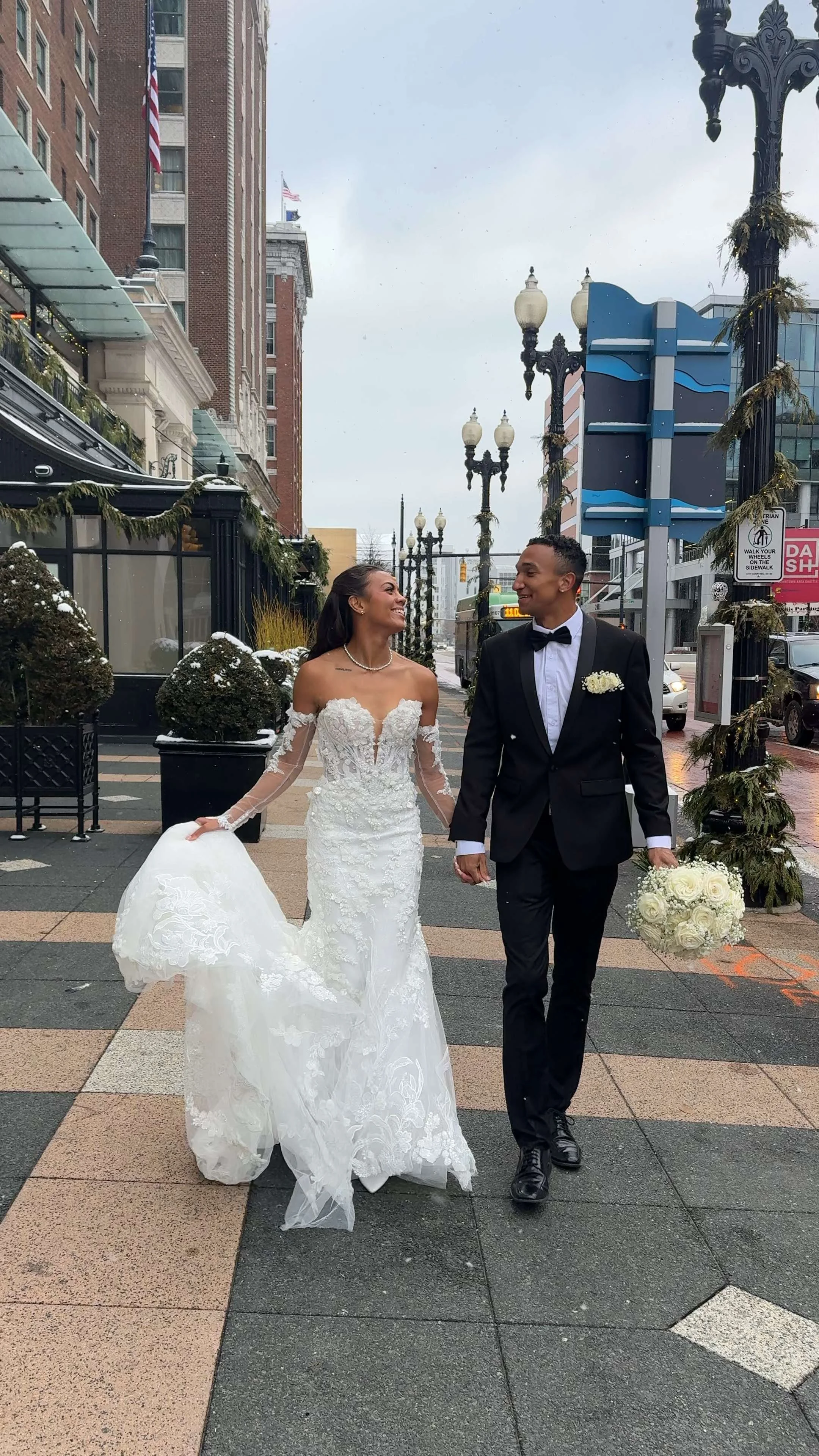 Wedding or special occasion table with white high-heeled shoes, wedding ring, invitation cards, stamps, tissue box, gift box, and decorative items, with sunlight streaming through a window overlooking greenery.