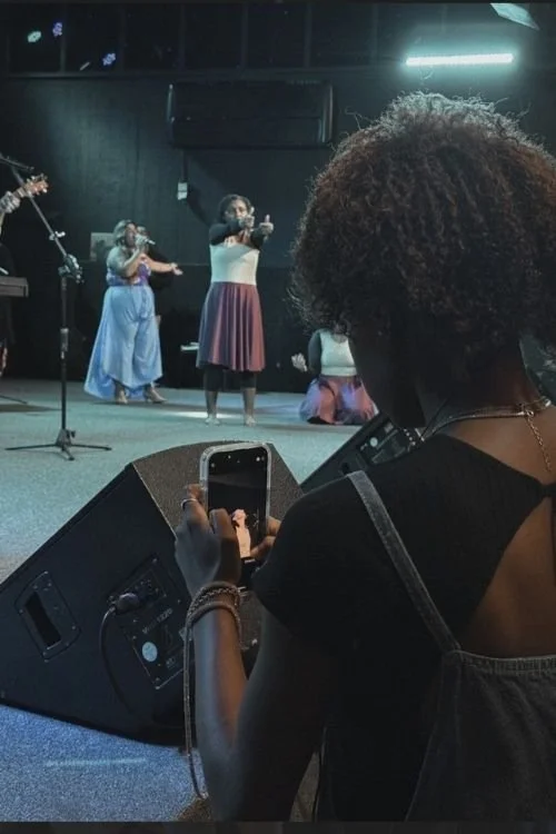 Silhouettes of a man and woman on stage with blue lighting; woman holding a microphone