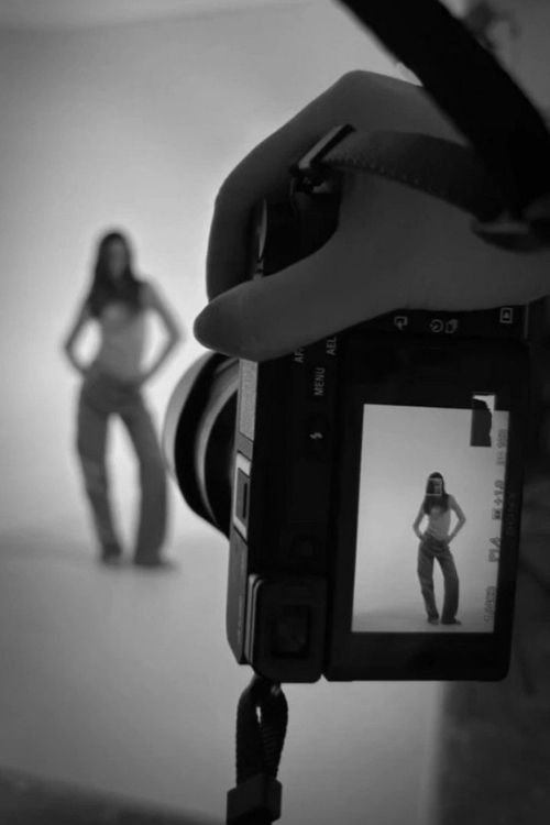 Concert venue with people sitting and standing, blue stage lights illuminating the stage, and cowboy boots, a hat, and a white cowboy hat resting on the seats in the foreground.