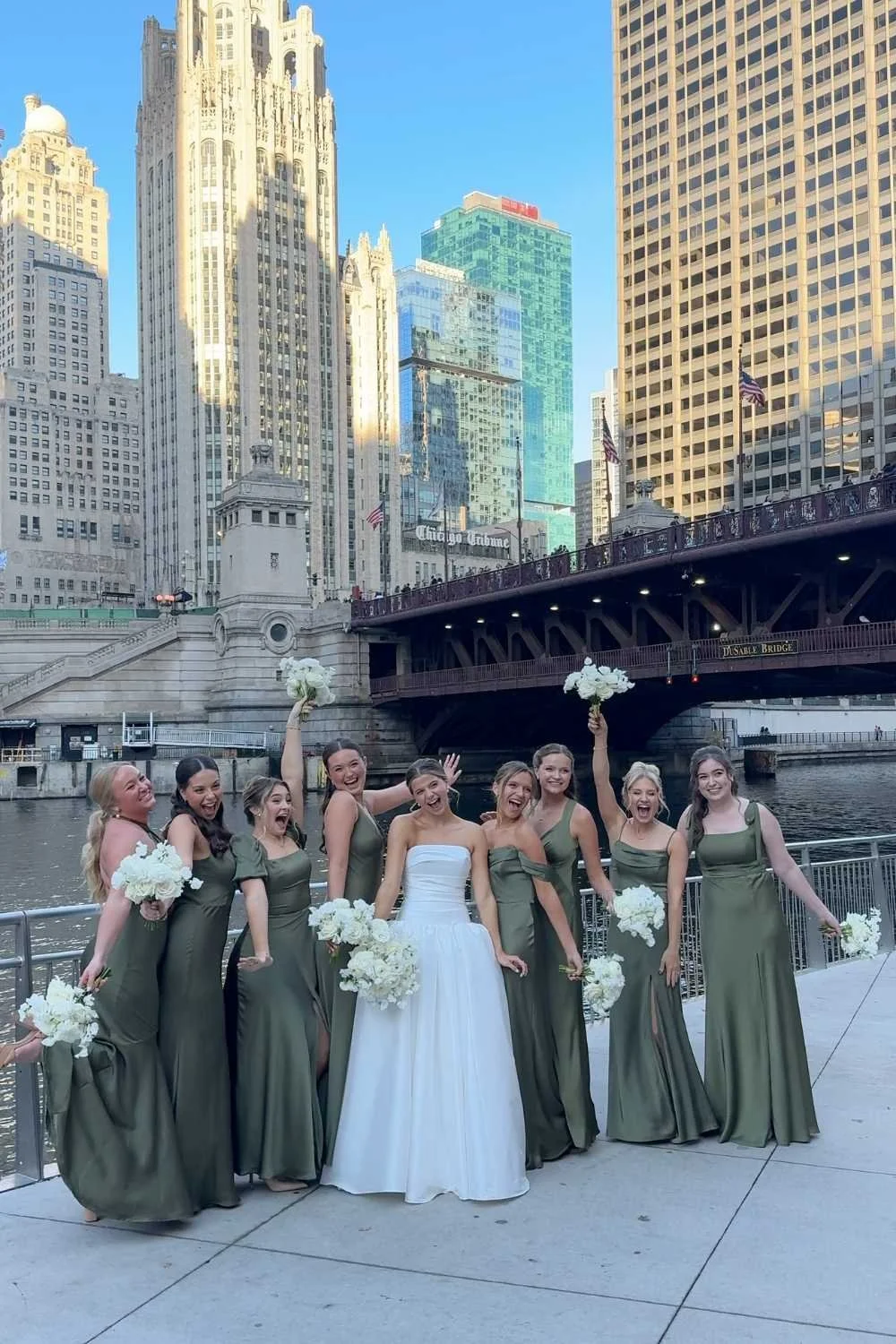 A woman in a white dress and a man in a gray suit and maroon turban dancing in a decorated indoor area with checkered black and beige flooring, greenery wall, and hanging lights, at a celebration or wedding.