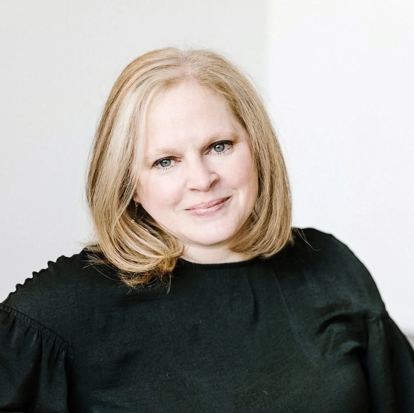 Jessica has shoulder length blonde hair styled in a bob. Pictured with a white background, Jessica is also wearing a black blouse.