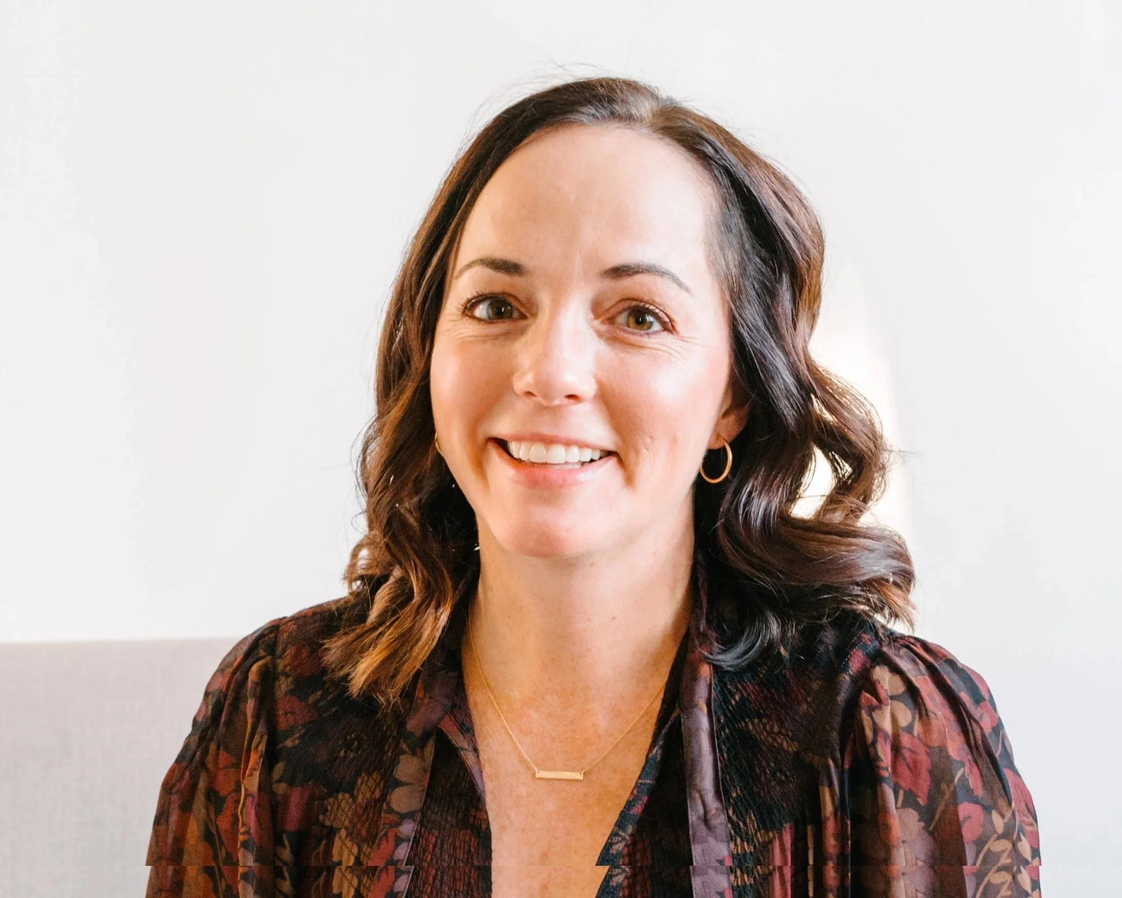 Quannah is pictured smiling wearing a black blouse with various flowers that have a fall theme.