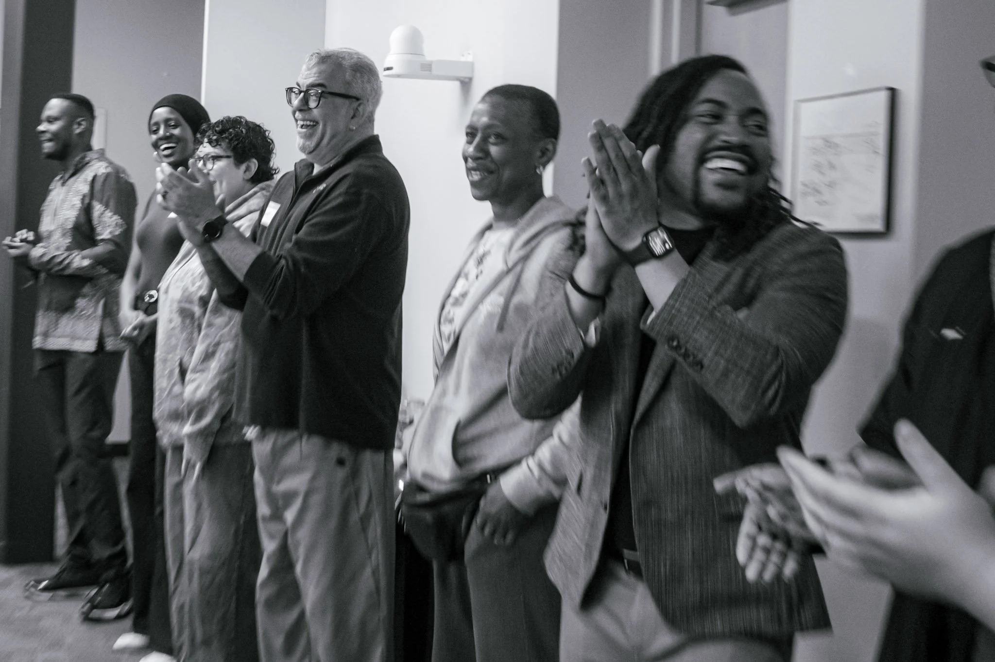 A group of diverse people standing in line, smiling and laughing, in an indoor setting.