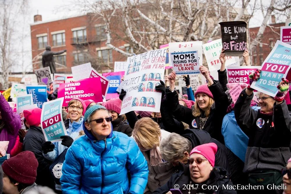 MomsRising and other organizations and community members hold signs advocating for paid family leave, empowering women, and other motifs at the Women's March in Concord, New Hampshire in 2017. Photo taken by Cory MacEachern Ghelli.