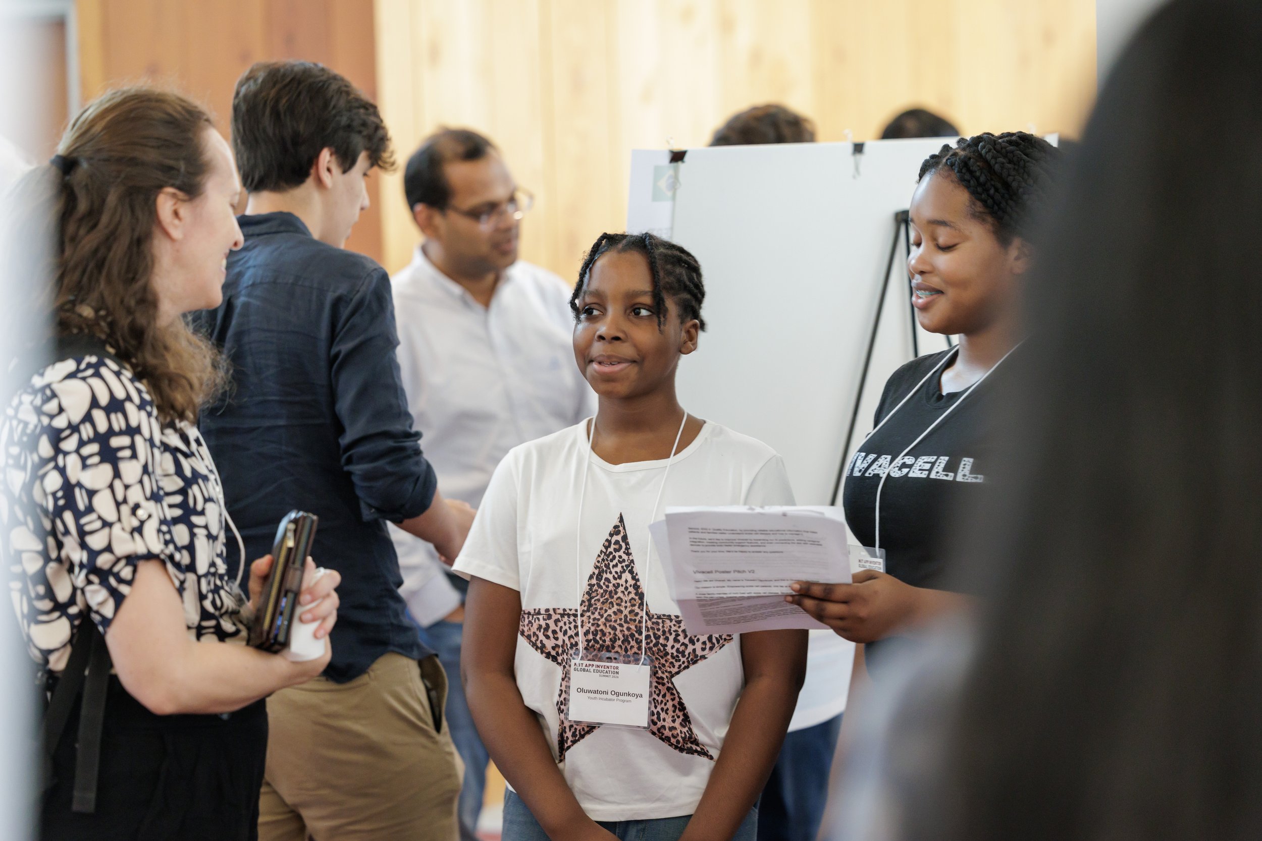 A group of young people engaged in conversation at an indoor event, with some holding papers and wearing badges.
