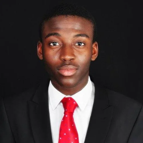 Portrait of a man in a suit and red tie against a black background.