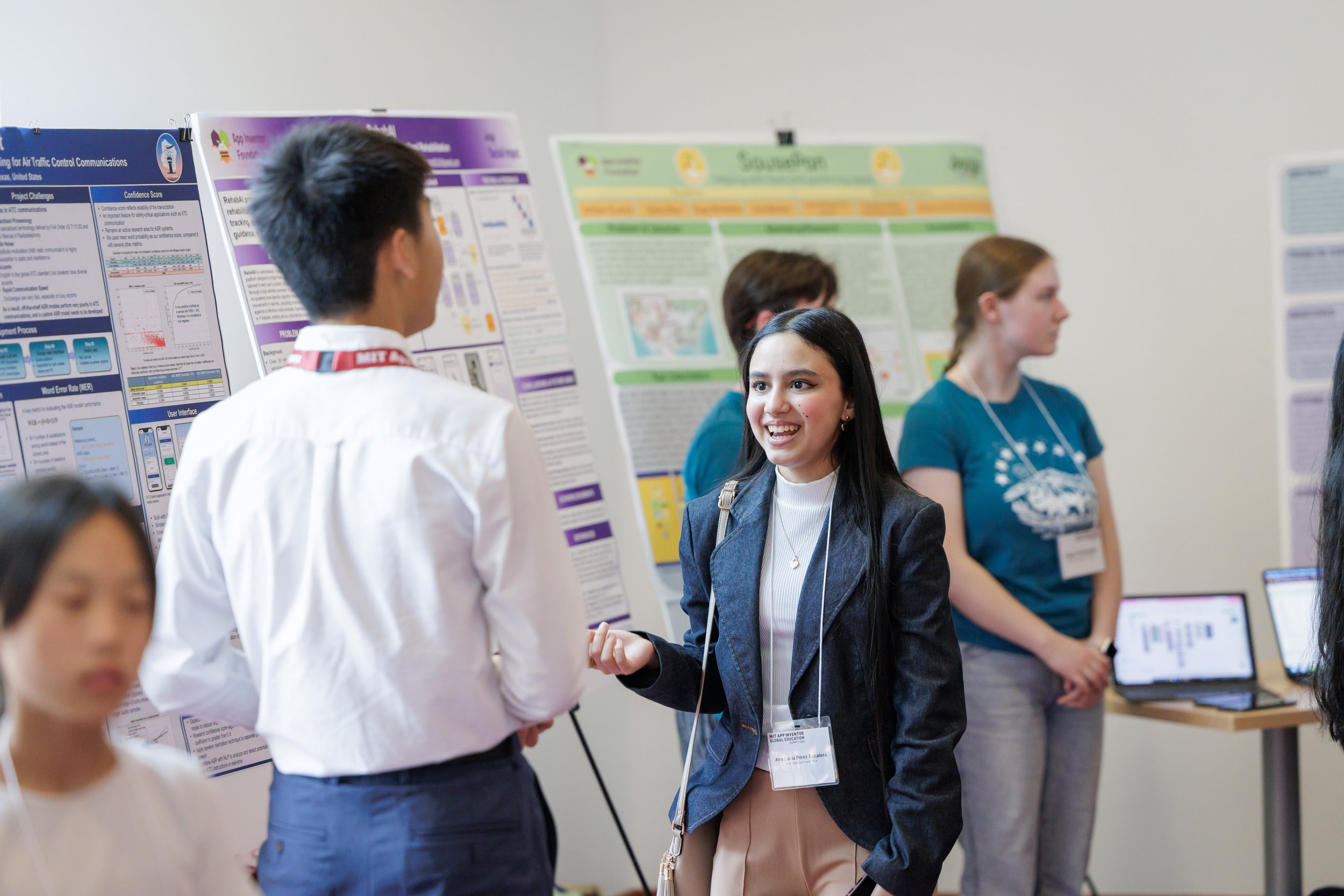 Group of young students at a science fair presenting research posters, with one girl smiling and talking to a boy.