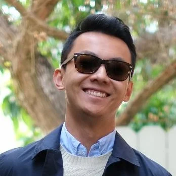 A man wearing sunglasses smiling outdoors with trees in the background.