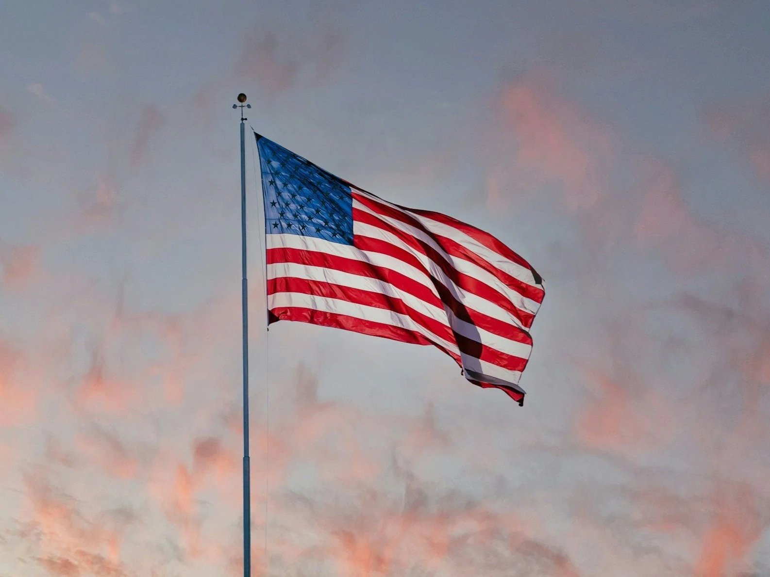 American flag waving on a tall flagpole against a pastel-colored sky at dusk.