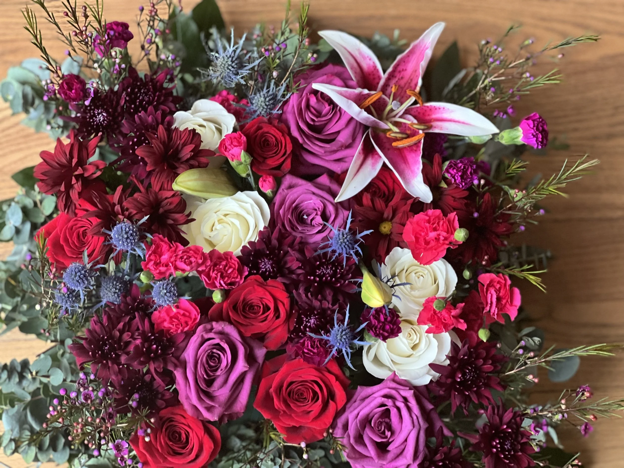Colorful floral arrangement with lilies, roses, and assorted flowers on wooden background.