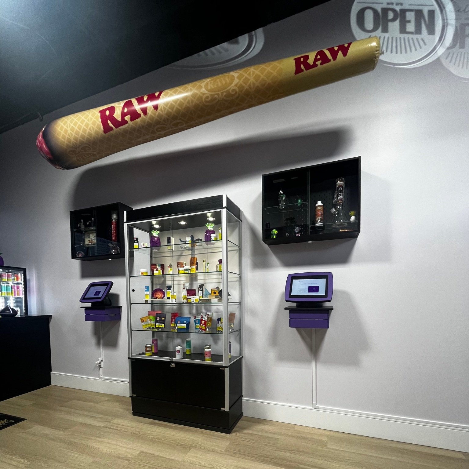 Inside the store view of a wall with a showcase and tablet screens to each side of it displaying the weed menus