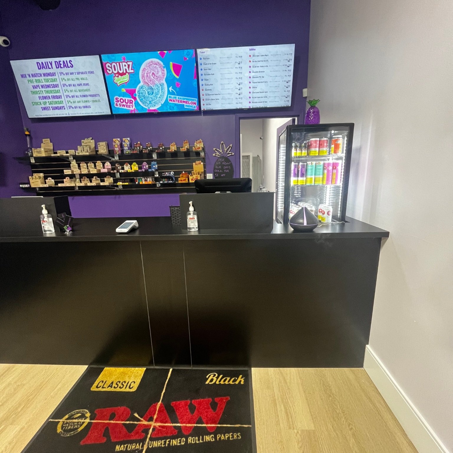 Inside the store view of Purple Pineapple Cannabis's front desk area with TV screens behind it showing the menus