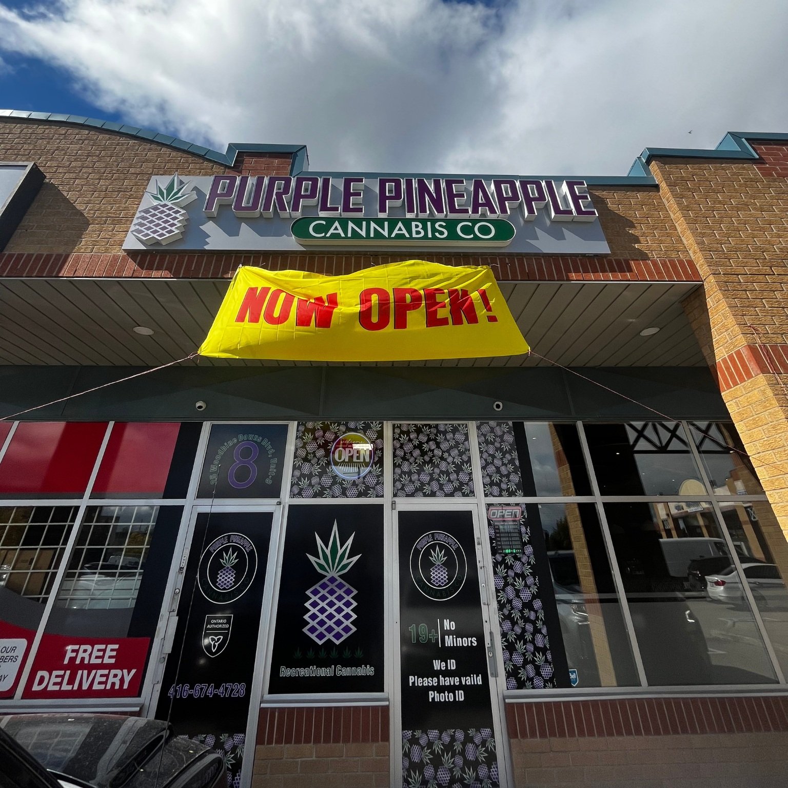 Entrance of Purple Pineapple Cannabis and a "Now Open" sign in yellow when the dispensary opened in 2022