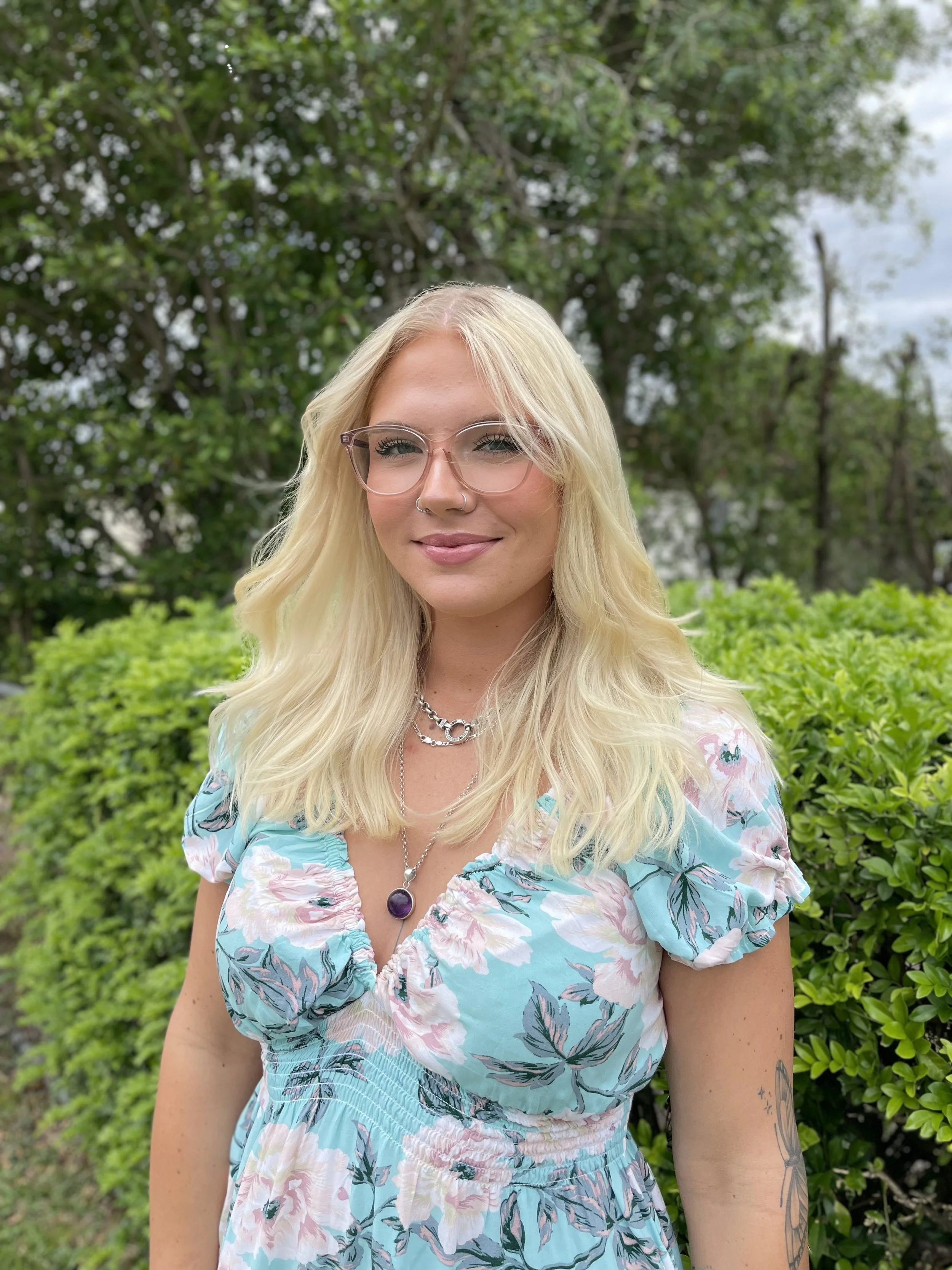 Smiling woman with blonde hair and glasses wearing a floral dress