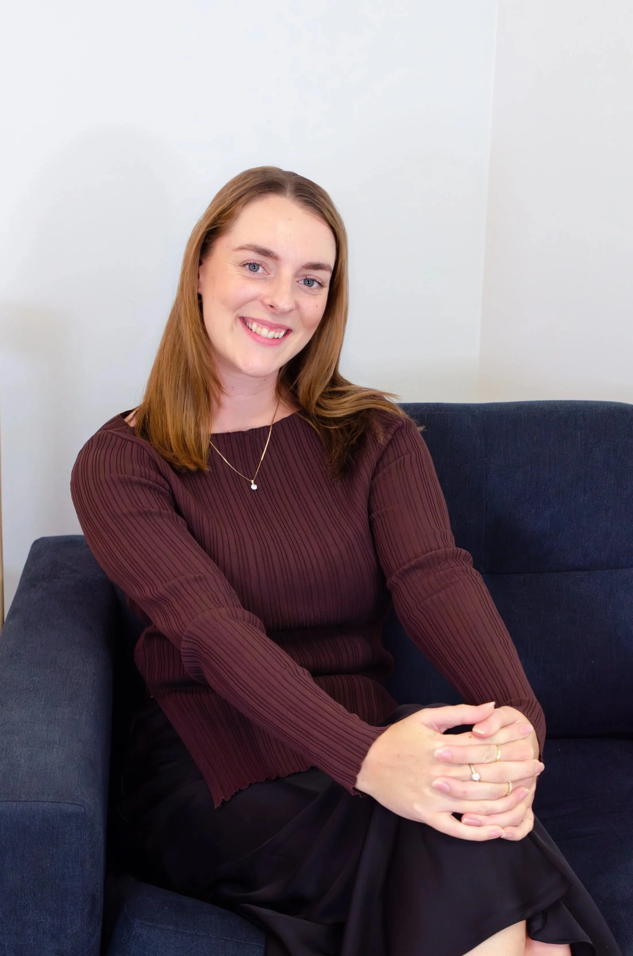Smiling woman with brown hair wearing a brown jacket and back shirt