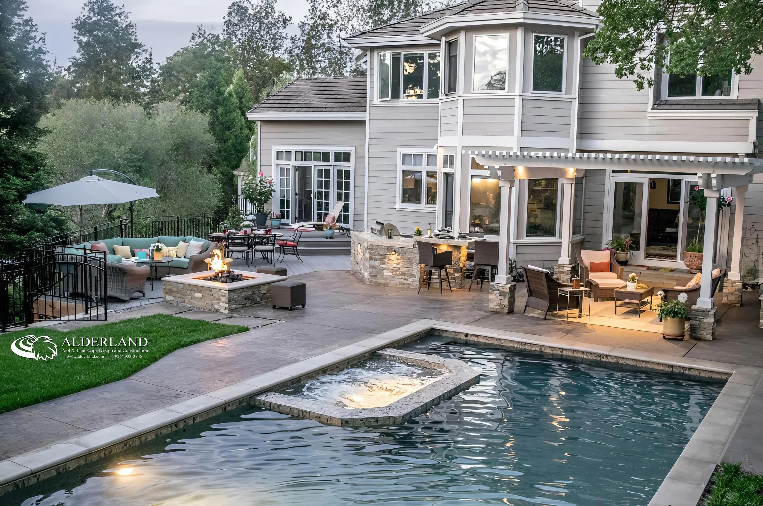 A spacious backyard with an in-ground pool, an outdoor seating area with a fire pit, a patio with a built-in bar, and a gray house with multiple windows and a balcony surrounded by trees.