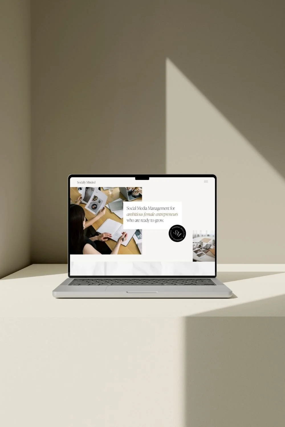 Laptop on a white table displaying a website about social media management for female entrepreneurs, with images of women working at a desk.