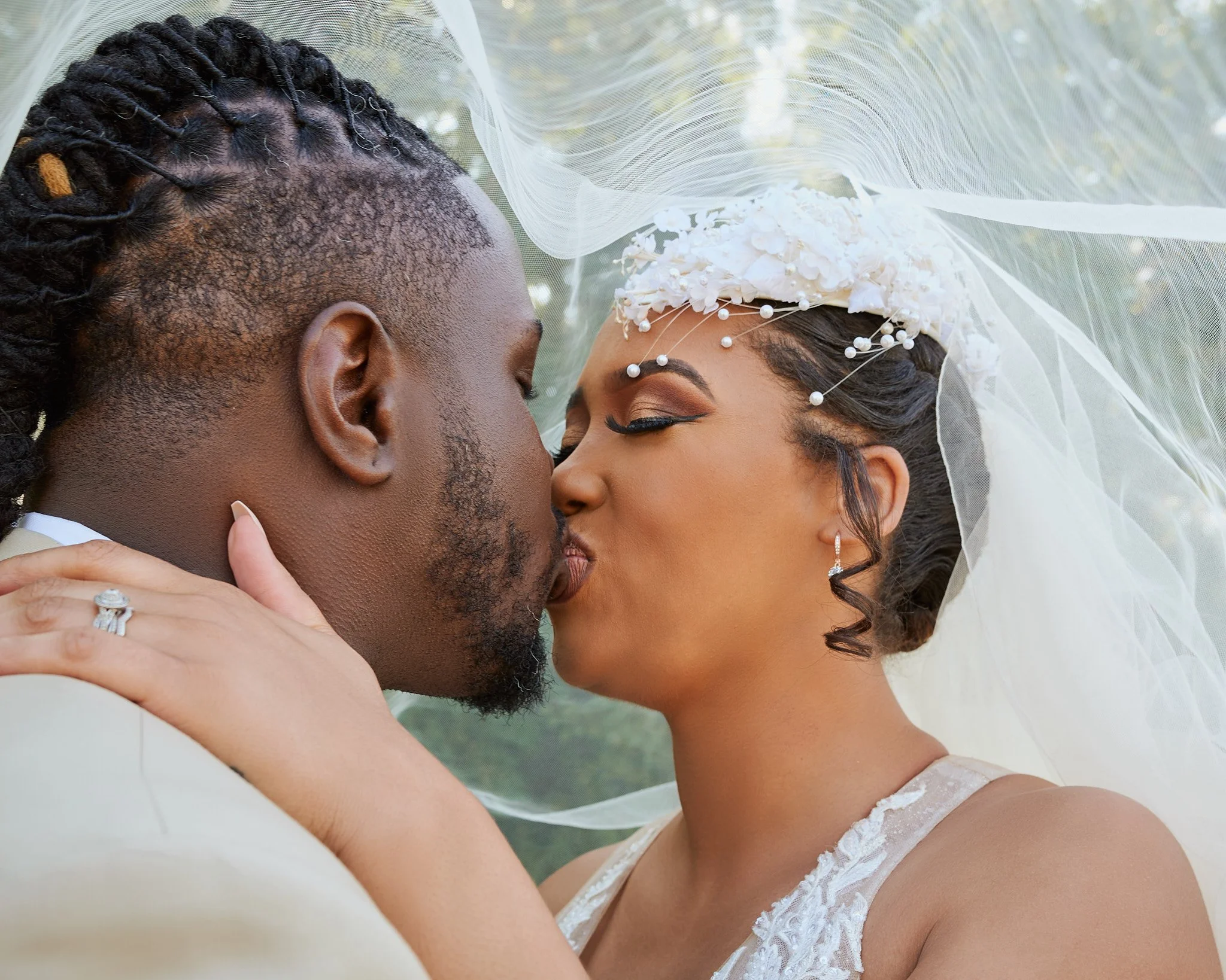 Couple sharing a kiss during their wedding, with the bride wearing a veil and floral headpiece, and the groom holding her face gently.