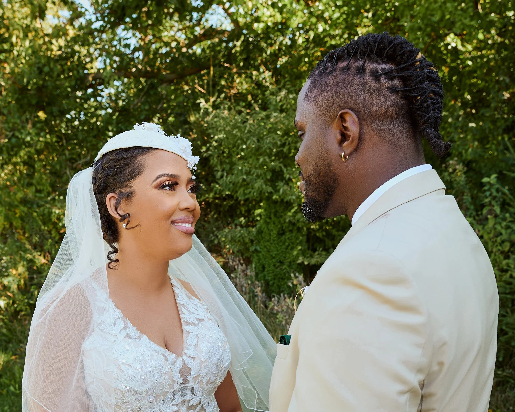 A bride and groom gazing at each other outdoors during wedding ceremony, with green foliage in the background.