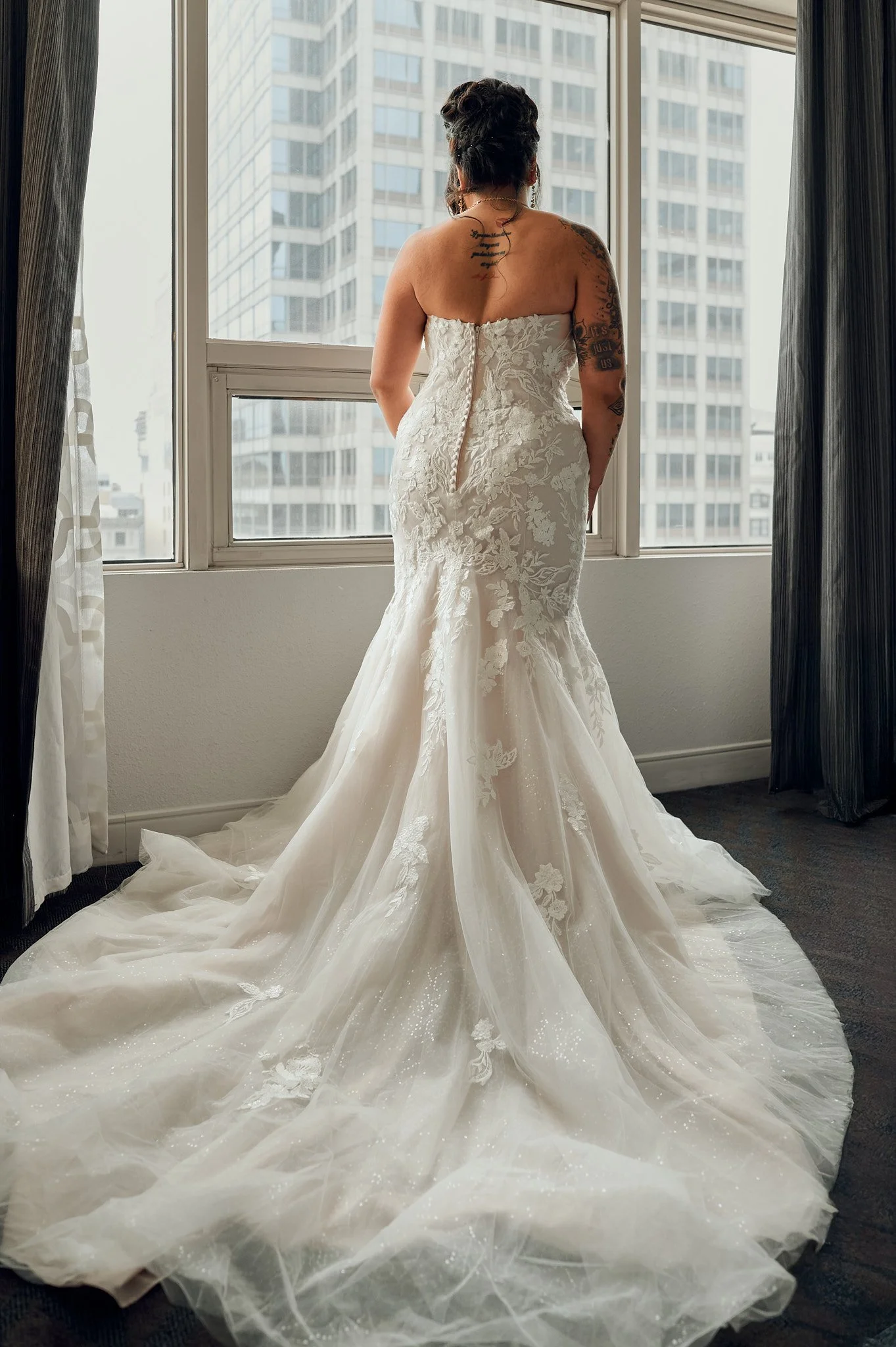 Woman in a wedding dress looking out of a window in a high-rise building.
