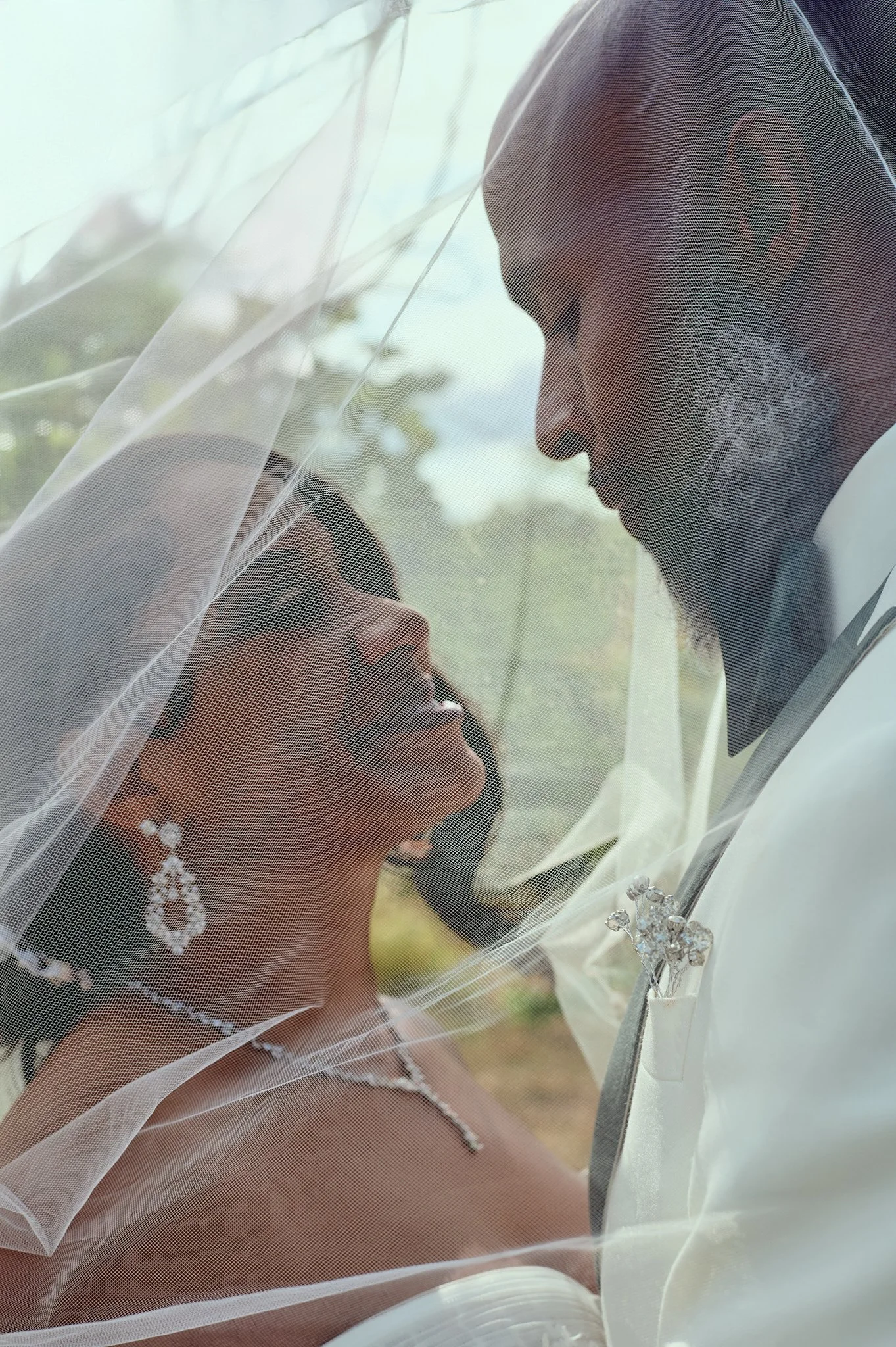 Bride and groom sharing a moment behind a sheer veil outdoors.