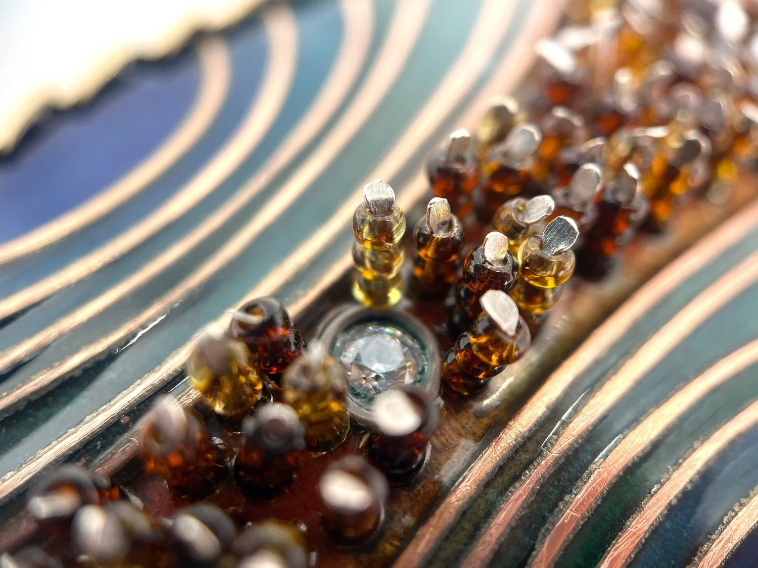 detail of handmade cloisonné  enamel brooch with blue and green arcs and amber beads