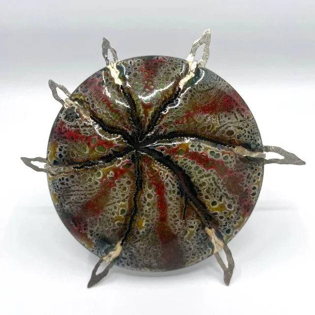 round handmade enamel brooch with brown and red pattern and cracks and pierced silver spikes