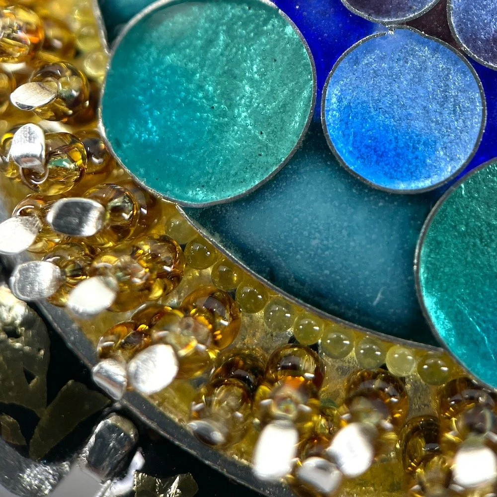 detail of round handmade cloisonné  enamel brooch with blue and green circles and amber beads