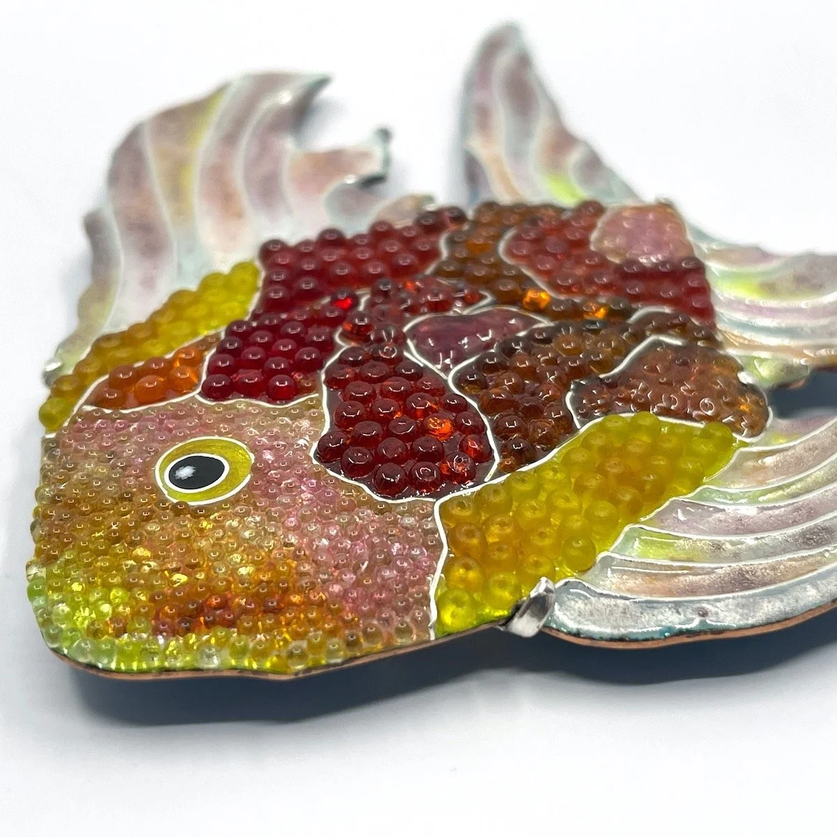 Close up of enamel and beaded fish cloisonné brooch in pinks, reds, and yellows