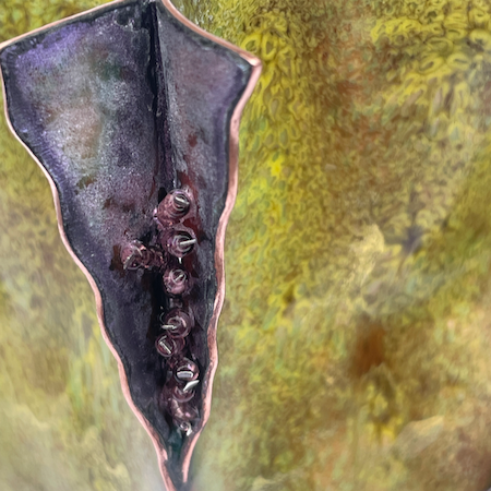 Close up of Small cut and shaped copper enamel bowl with fins in green and purple with gold shimmer and beads