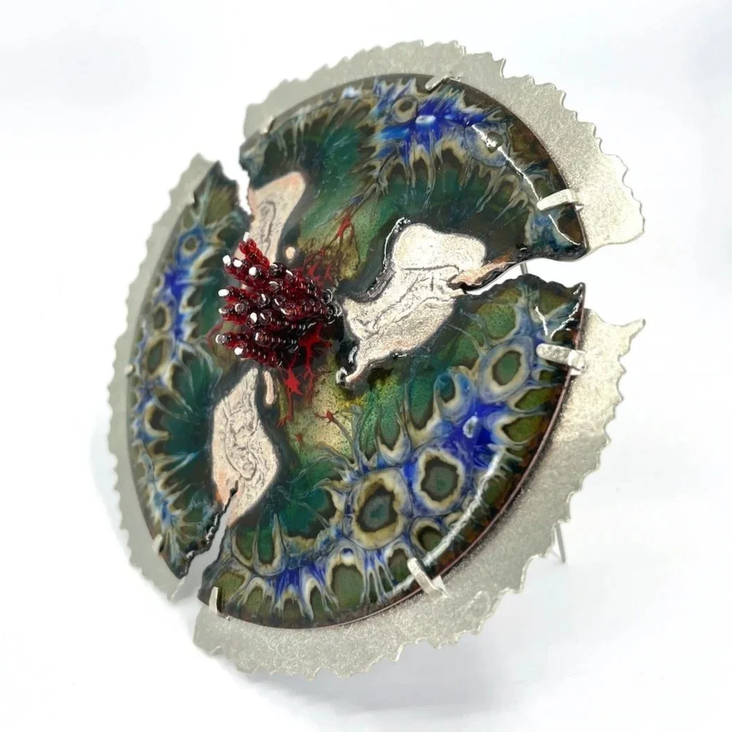 round handmade enamel brooch with blue and green pattern and silver areas and red beads