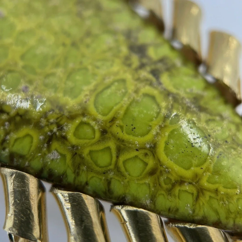 Close-up of green marquise enamel brooch with curly brass setting