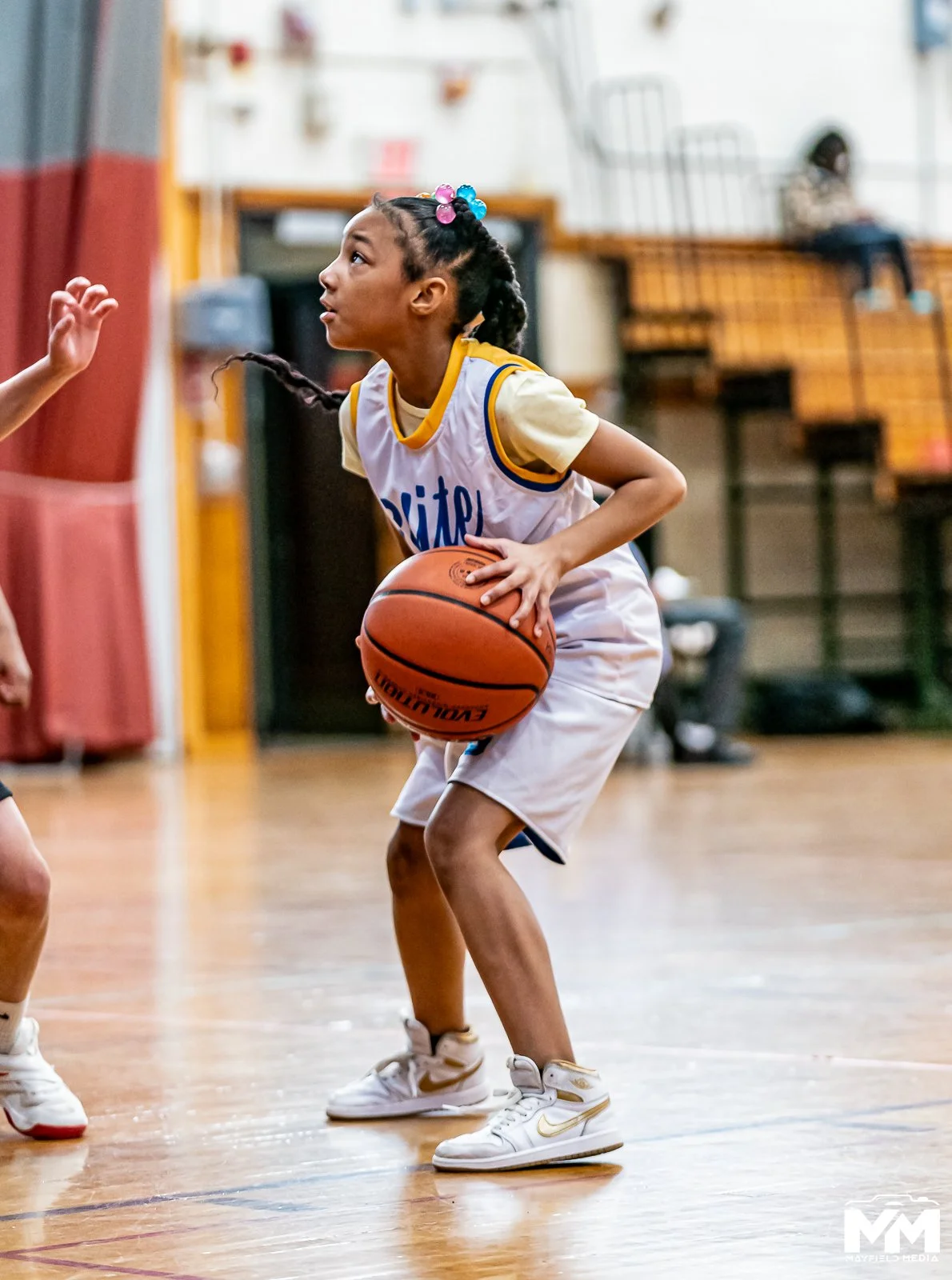 A young girl playing basketball inside a gym, holding a basketball and preparing to make a move on the court.