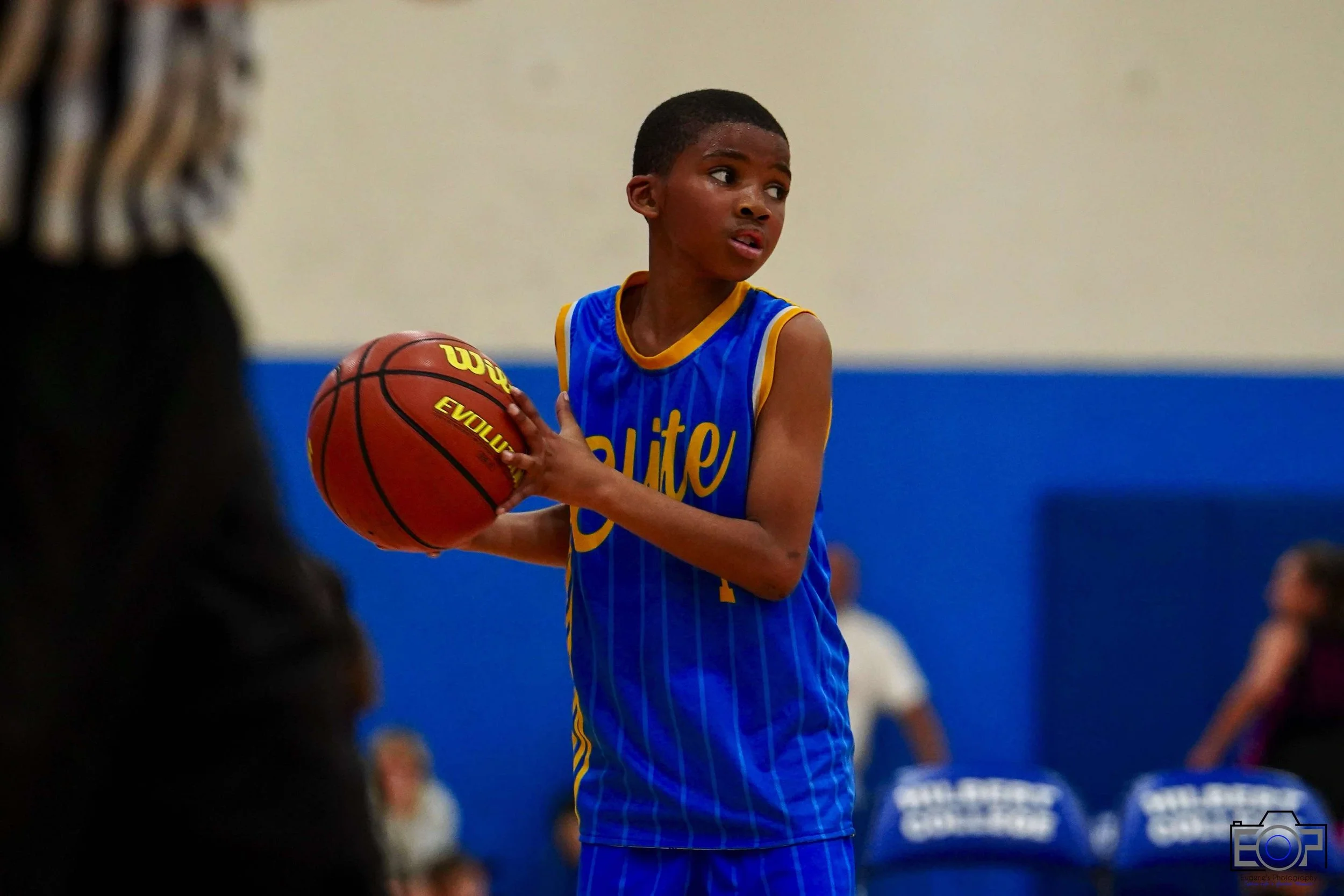 Young basketball player in blue uniform practicing in gymnasium with hardwood floor.