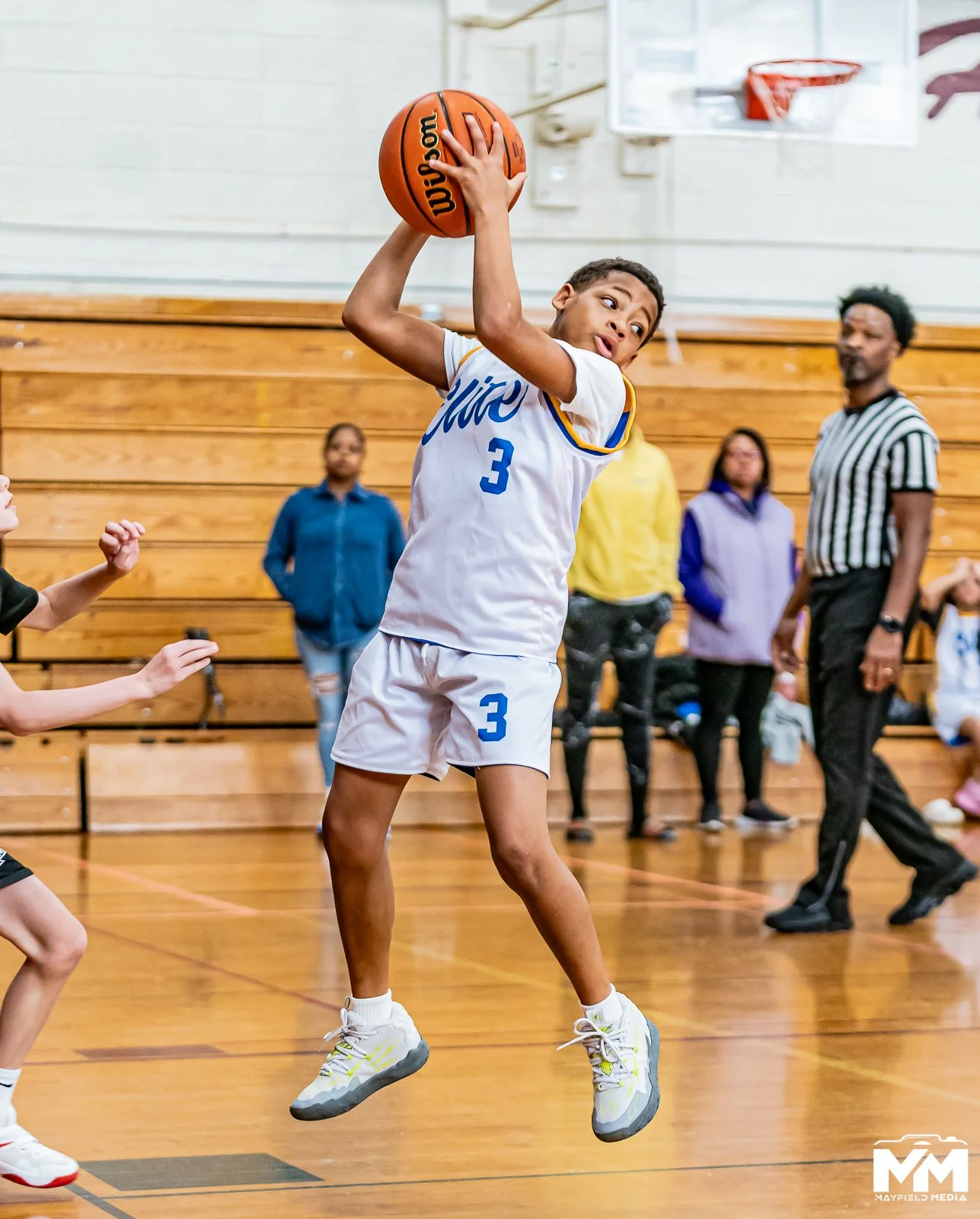 Young girl with braided hair and athletic clothing reaching for a basketball during a game or practice in a gymnasium.