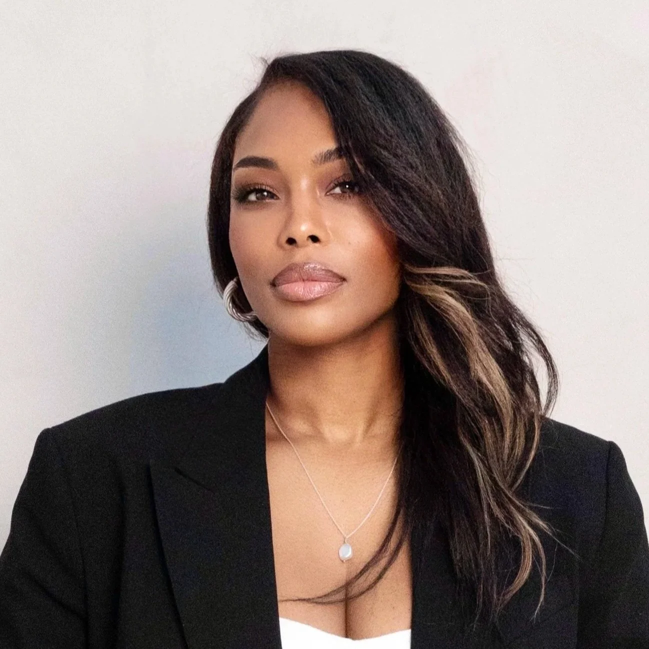 Woman smiling in a black blazer, wearing a white blouse