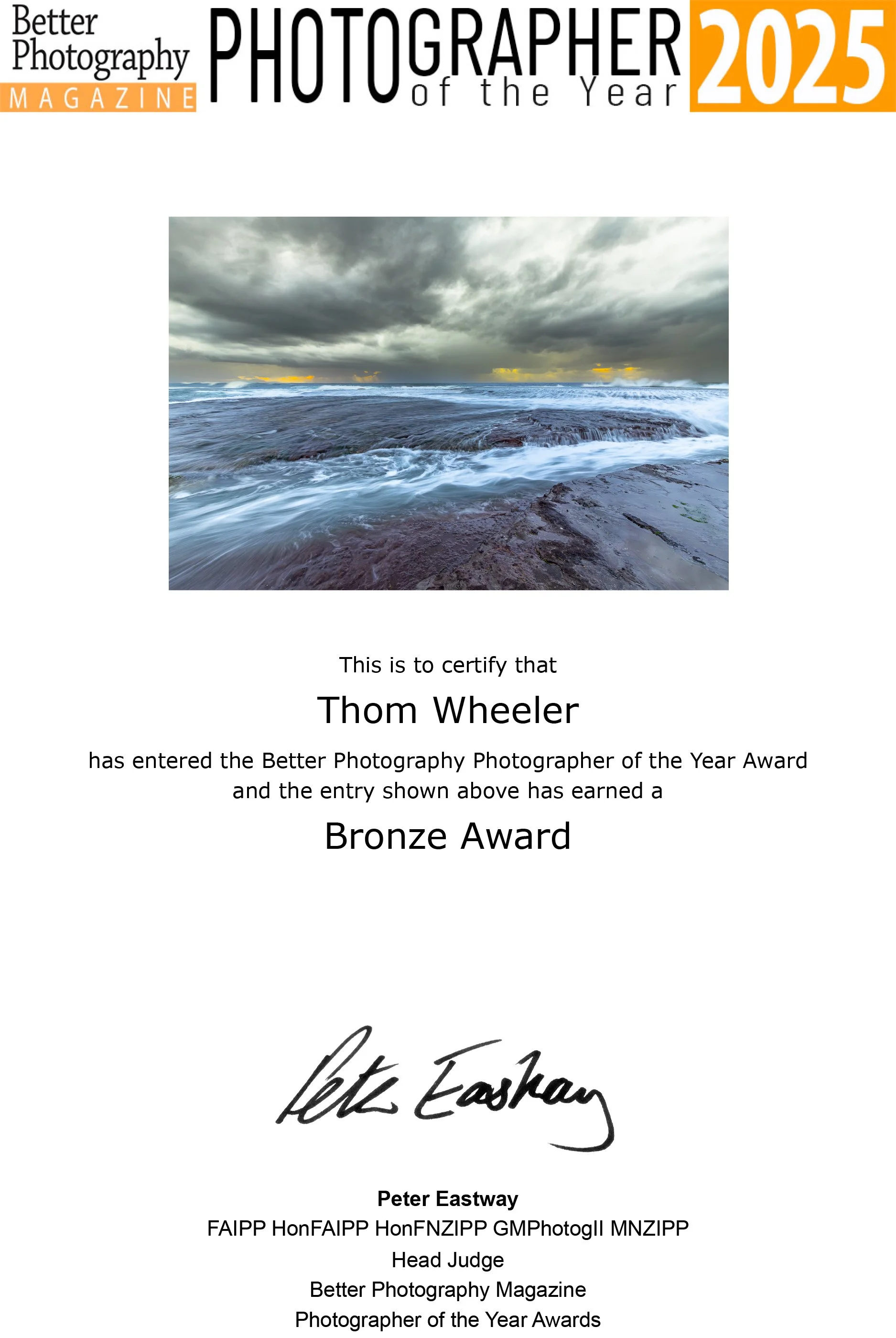 Certificate of Achievement awarded to Thom Wheeler for entering the Better Photography Photographer of the Year 2025, featuring ocean with waves crashing onto rocks under dark, stormy skies at sunset or sunrise.