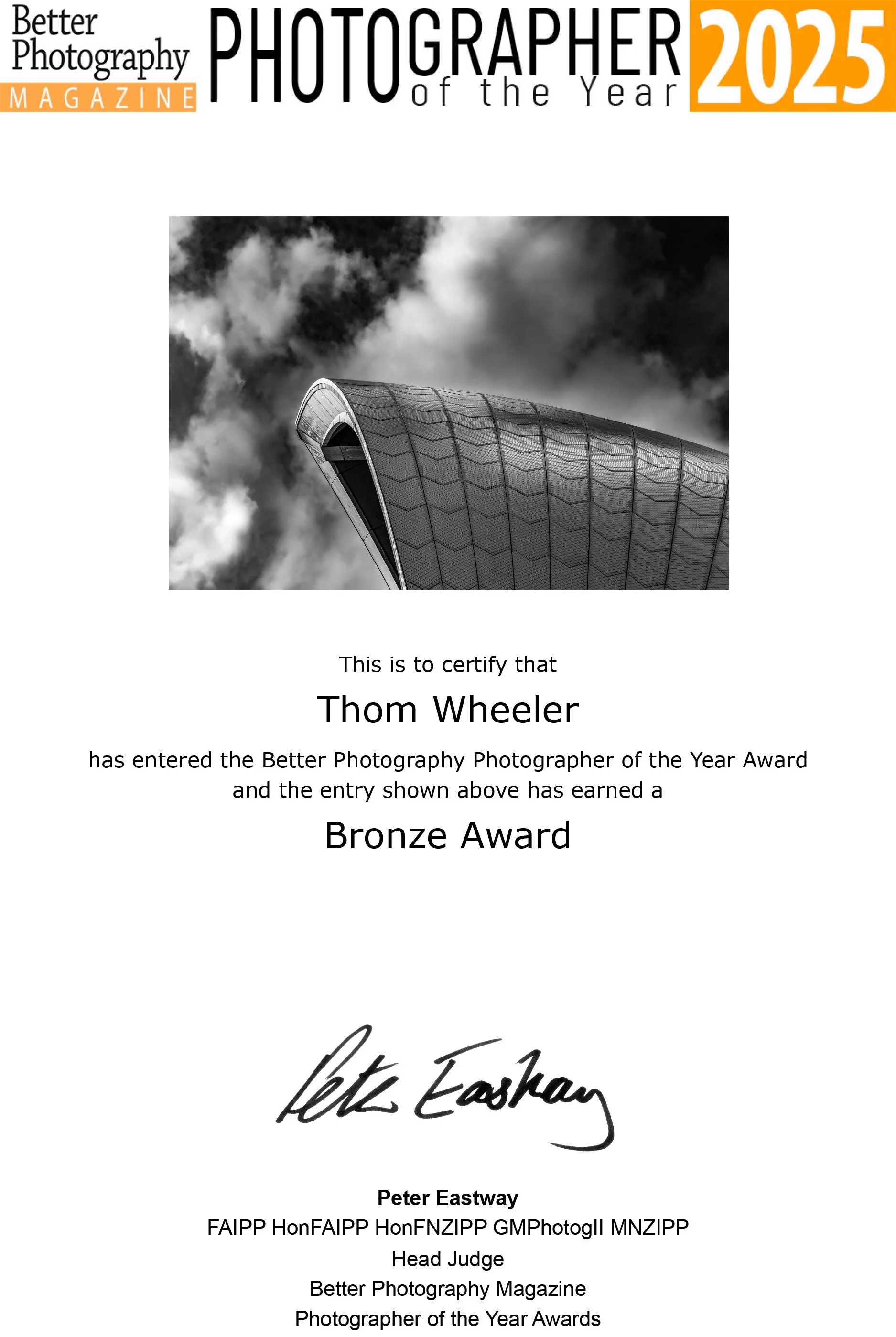 Certificate of achievement for Thom Wheeler, awarded the Bronze Award for Photographer of the Year 2025 by Better Photography Magazine, featuring a black-and-white photograph of a modern architectural building with a curved roof against a background of dramatic clouds.