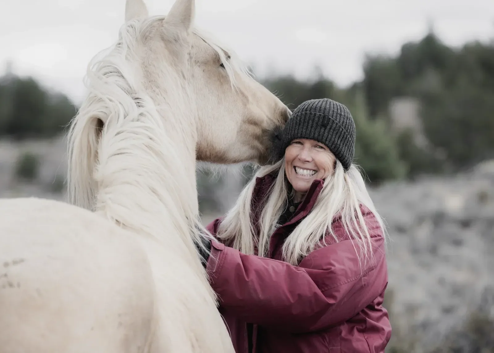 Angela smiling as a white rescue horse affectionately nuzzles her face at Broken Arrow Ranch and Sanctuary.